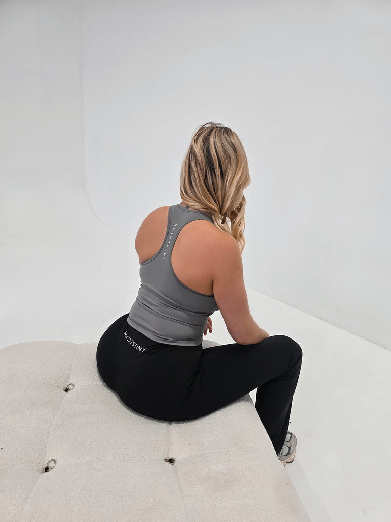Woman sitting on a white ottoman wearing black leggings with a visible brand logo.
