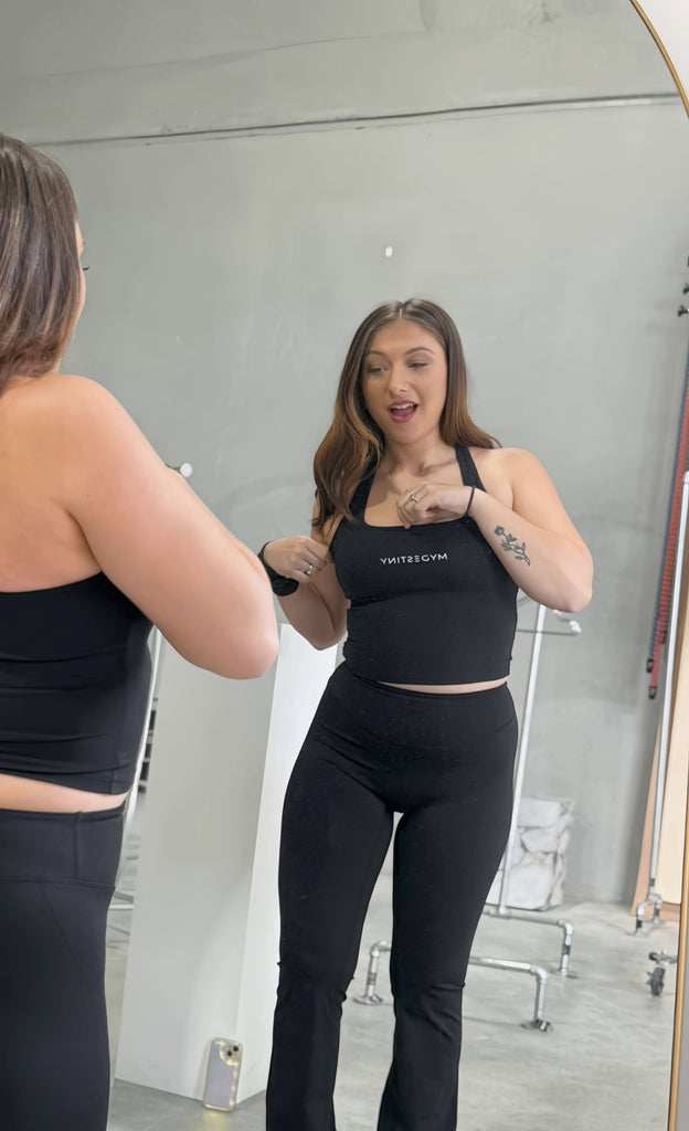 Woman trying on a black sports bra and leggings in front of a mirror.
